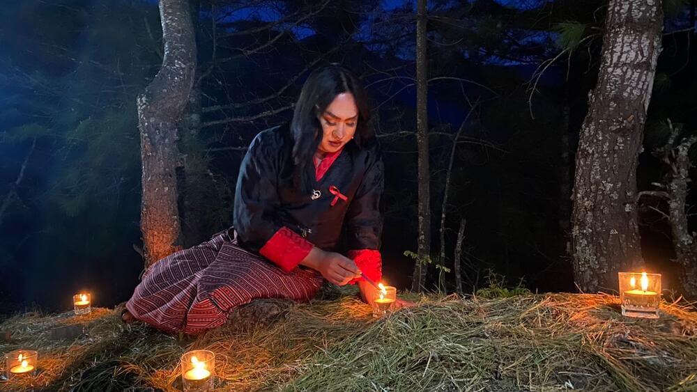 Tshering wears traditional Bhutanese attire and wears a red ribbon to light candles.