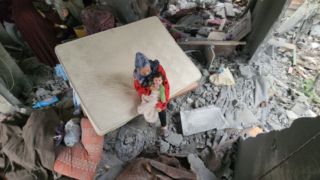 Mother and baby sit in rubble in Gaza.